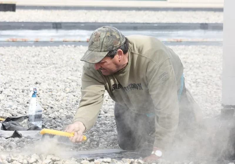 A worker repairs roofing on a local high school after a storm.