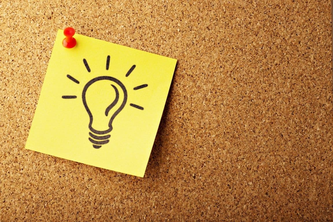 A post-it note with a lightbulb drawn on it on a cork bulletin board.