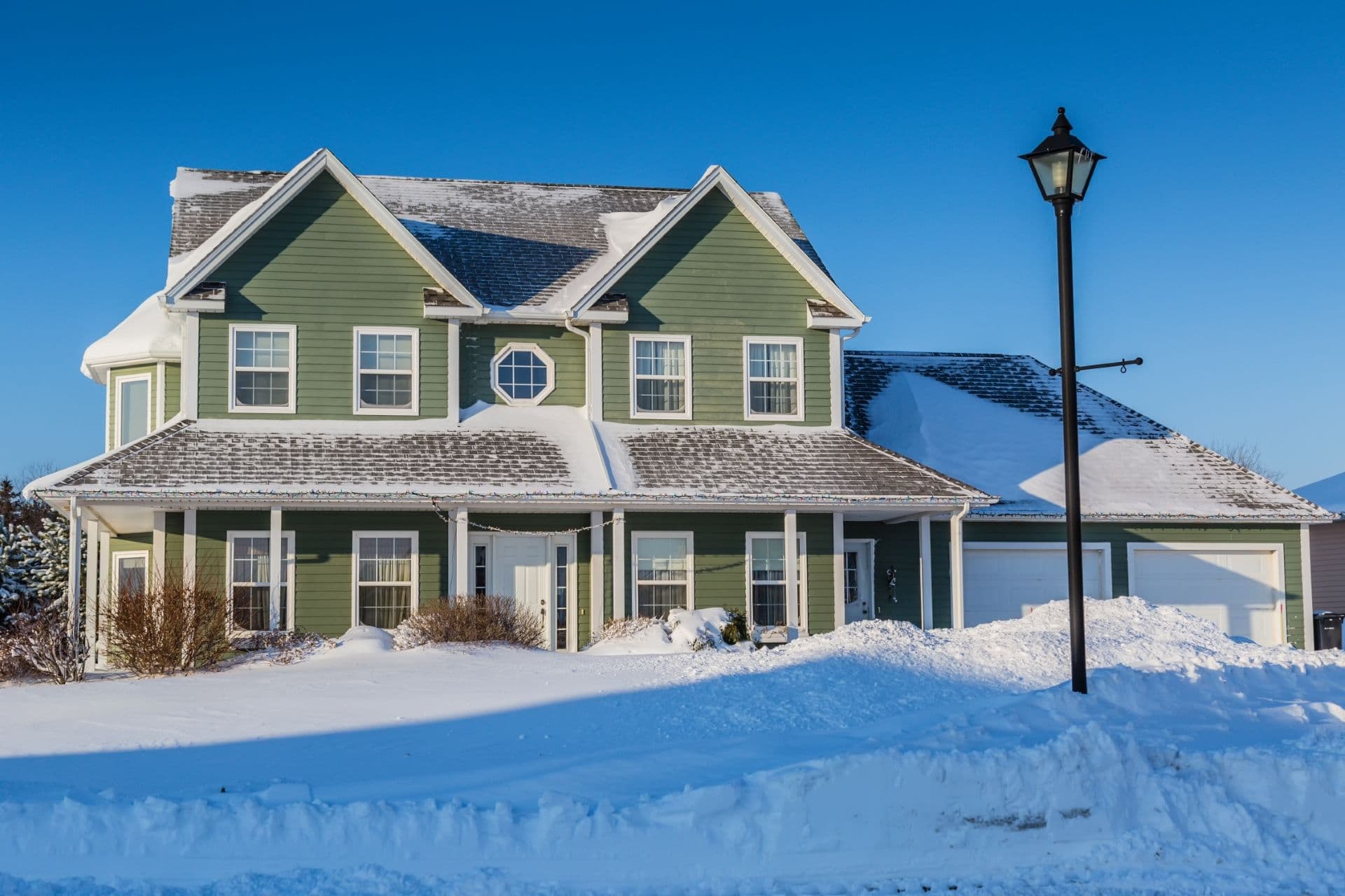 A green house with white trim covered in snow.