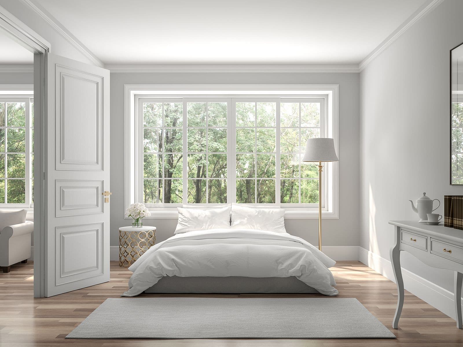 A light gray bedroom with large double-hung windows and a floor lamp.