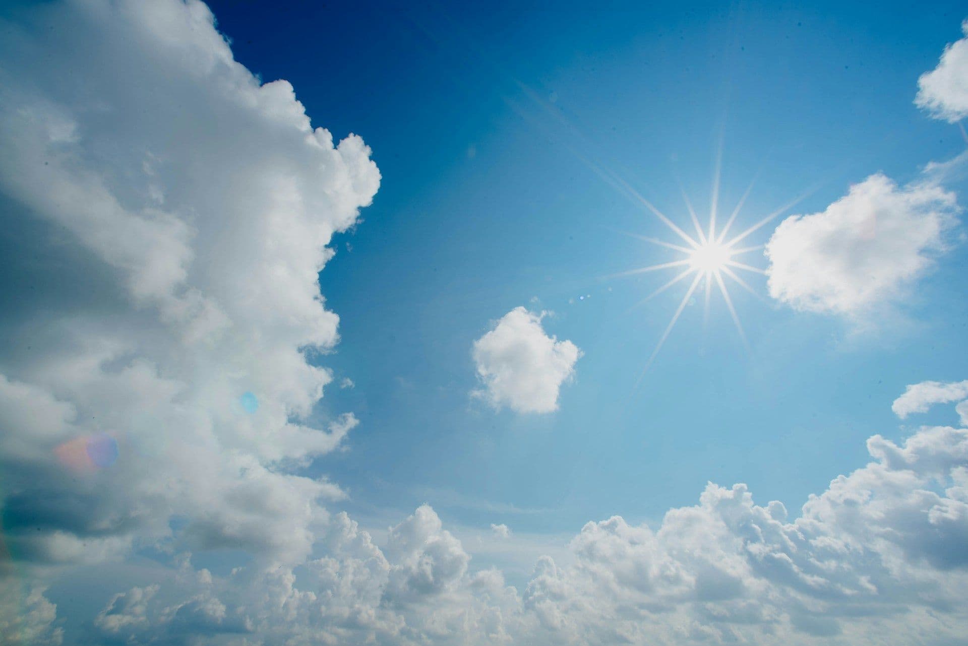 The sun in a blue sky with clouds.