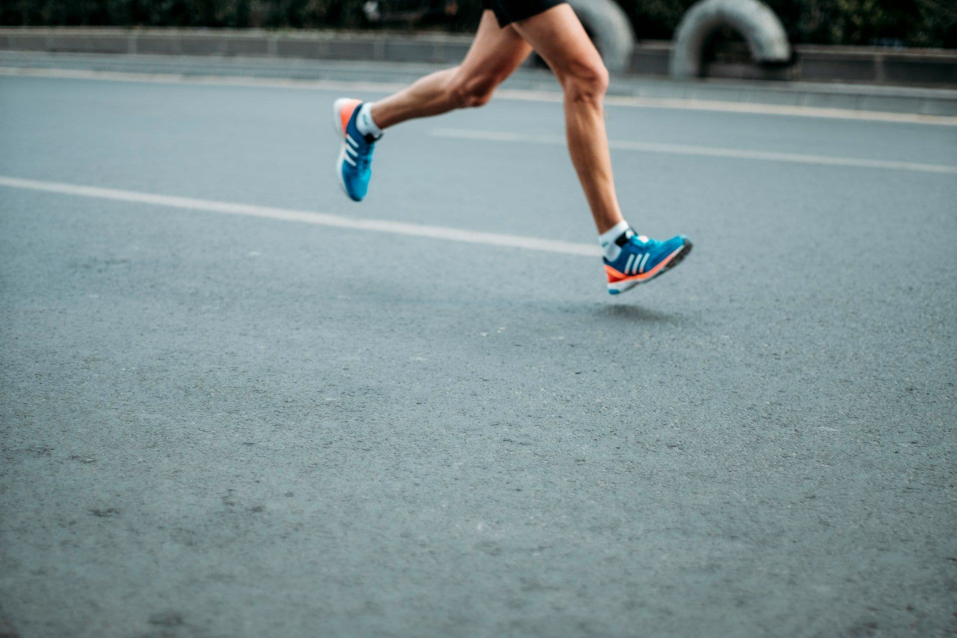 A person in blue sneakers runs on pavement.