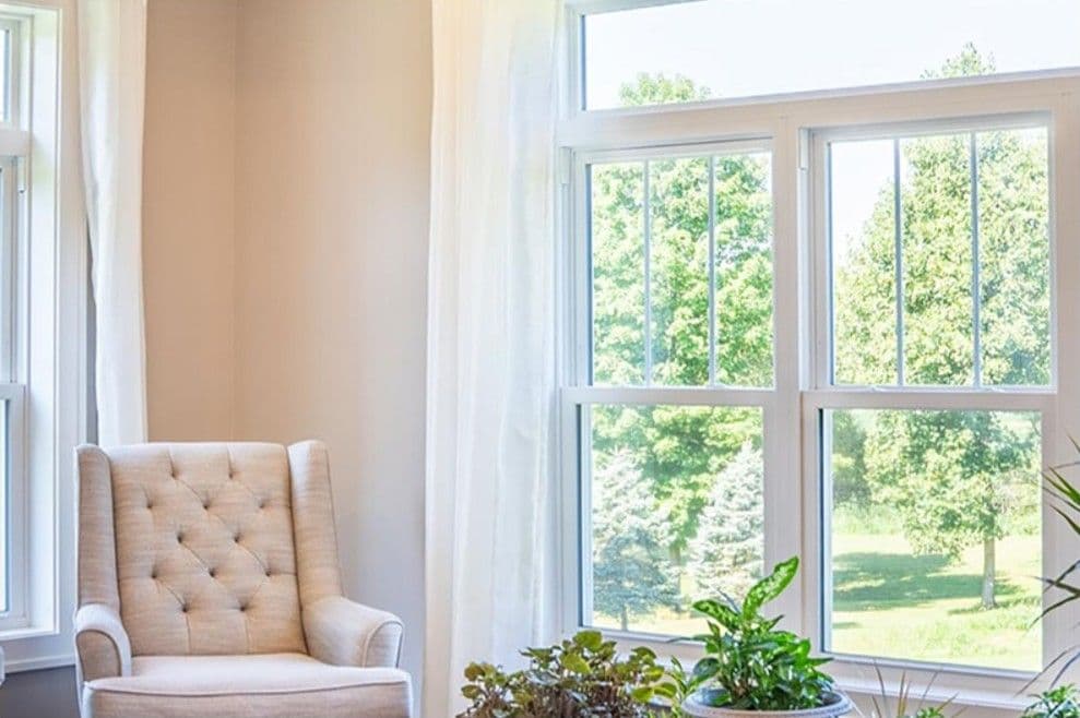 A beige armchair sits beside large double-hung windows.